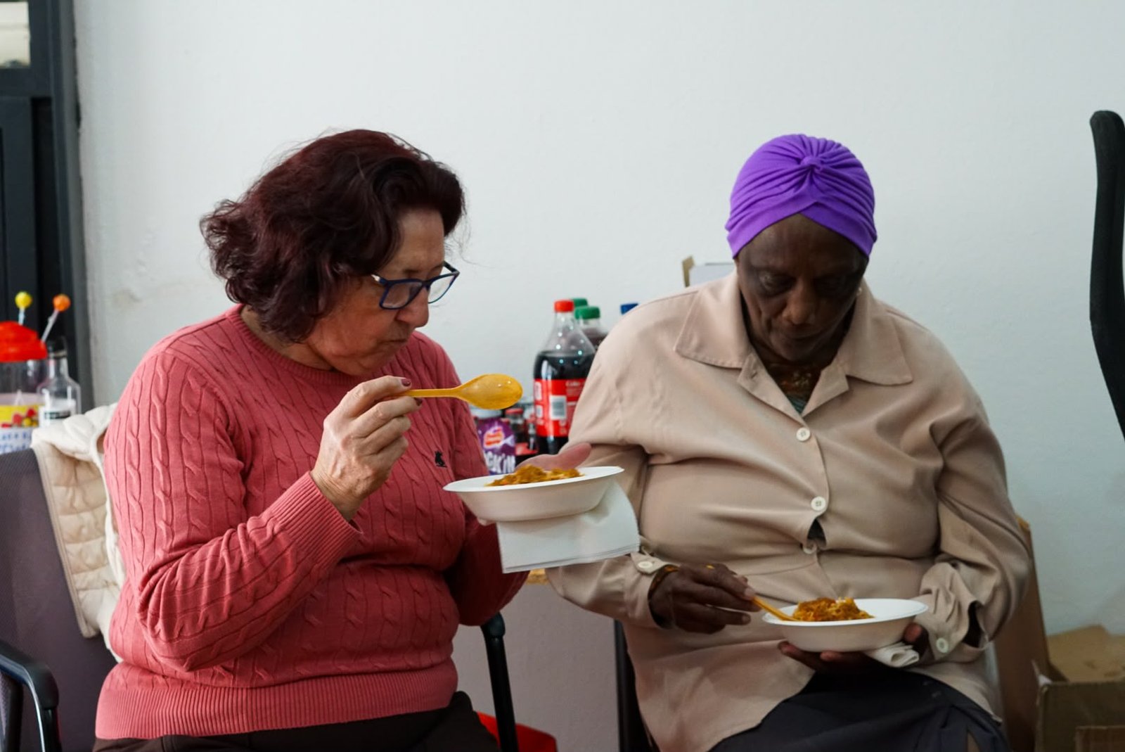 Duas senhoras sentadas a provar comida em pratos de papel